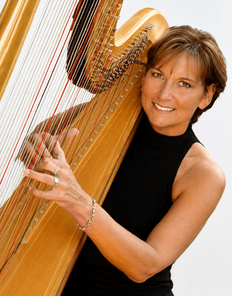 Smiling woman in a black sleeveless top plays a wooden harp, showcasing her hands poised on the strings, highlighting her musical talent.